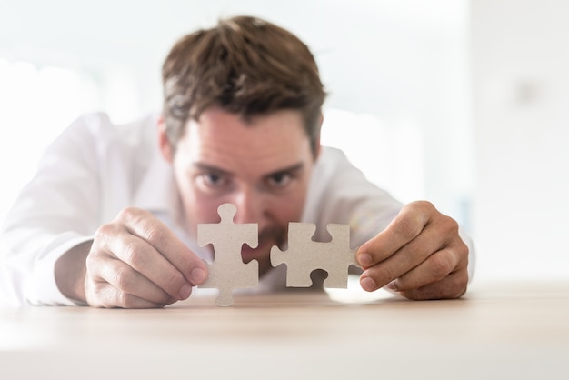 Jeune homme d'affaires s'appuyant sur son bureau joignant deux pièces de puzzle assorties.