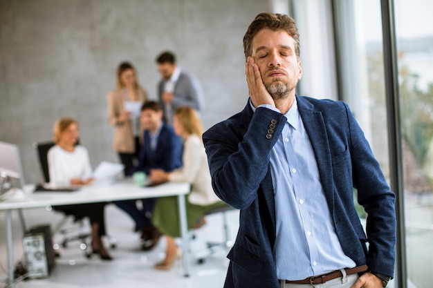 Jeune homme d'affaires se sentant épuisé et debout sur son lieu de travail au bureau