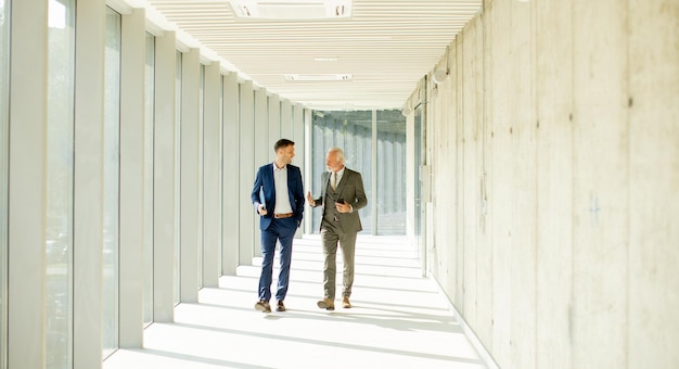 Un jeune et un homme d'affaires senior marchent dans un couloir de bureau en pleine conversation