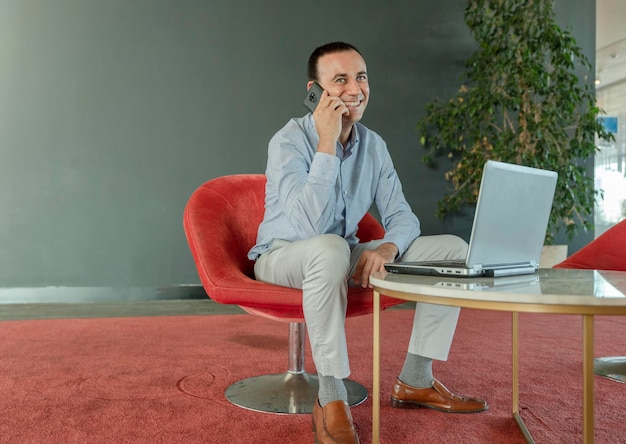 Un jeune homme d'affaires souriant assis au bureau, parlant au téléphone portable Concept d'entreprise de bureau mobile indépendant