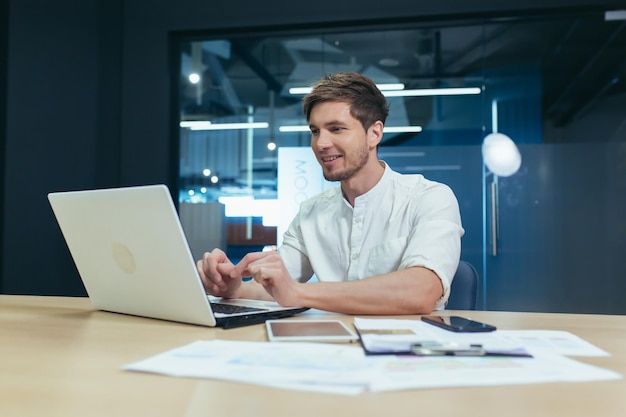 Jeune homme d'affaires souriant travaillant avec un ordinateur portable dans un bureau moderne en vêtements décontractés