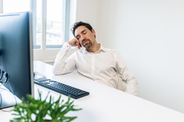 Jeune homme d'affaires surmené dormant à son bureau s'appuyant sur sa main.