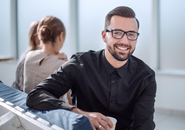 Jeune homme d'affaires avec une tasse de café assis dans un bureau moderne