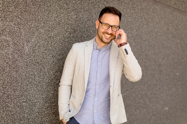 Jeune homme d&#39;affaires avec téléphone portable par le mur gris