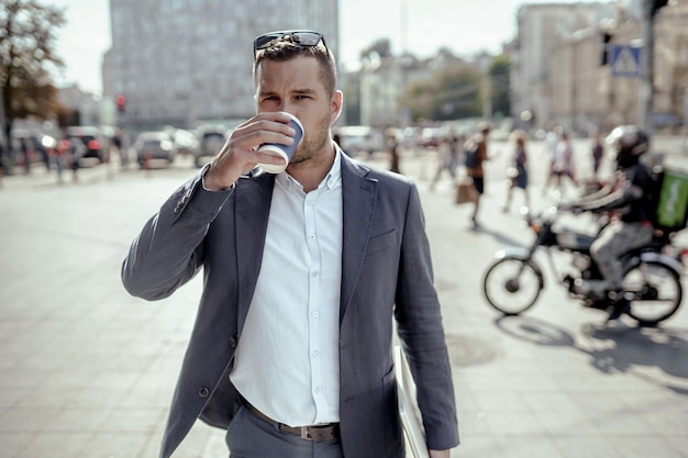 Jeune homme d'affaires tenant son ordinateur portable en buvant du café. Debout dans la rue.