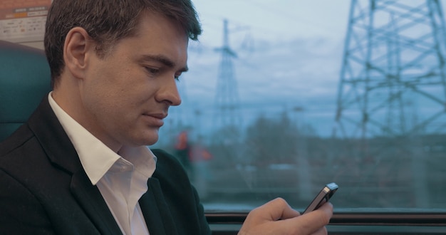 Jeune homme d'affaires textos sur smartphone lors d'un voyage en train