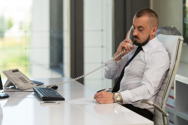 Jeune homme d'affaires travaillant sur son ordinateur tout en parlant au téléphone