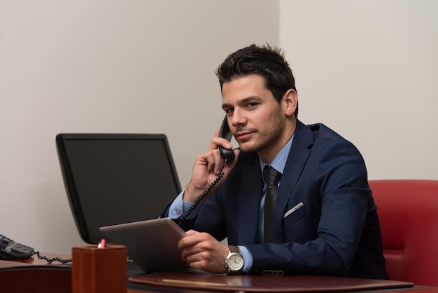 Jeune homme d'affaires travaillant sur son ordinateur tout en parlant au téléphone