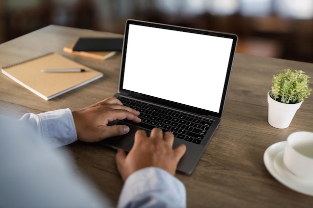 Un jeune homme d'affaires travaille sur l'ordinateur portable à l'aide d'un ordinateur de bureau avec un écran vide et un écran d'espace de copie vide