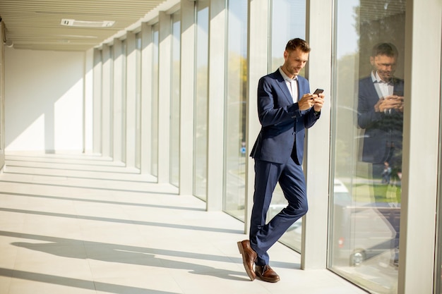 Jeune homme d'affaires utilisant un téléphone portable dans le couloir de bureau moderne