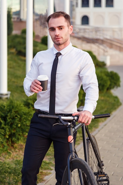 Jeune homme d'affaires à vélo boire du café de la tasse à emporter