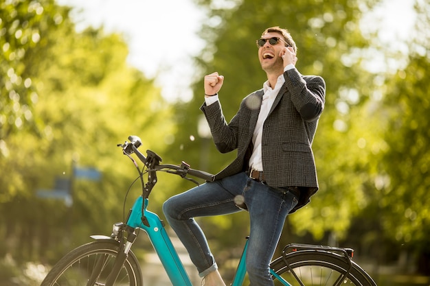 Jeune homme d'affaires sur le vélo électrique à l'aide de téléphone mobile