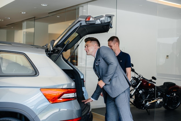 Un jeune homme d'affaires avec un vendeur examine le coffre d'une nouvelle voiture chez un concessionnaire automobile. Acheter une voiture.