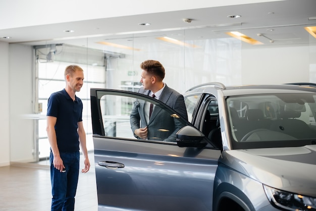 Un jeune homme d'affaires avec un vendeur regarde une nouvelle voiture chez un concessionnaire automobile. Acheter une voiture.