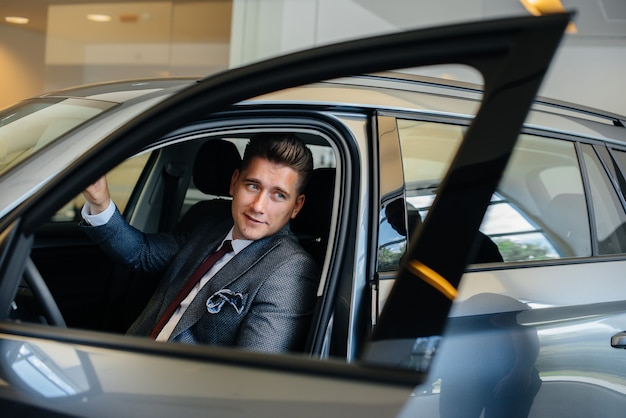 Un jeune homme d'affaires avec un vendeur regarde une nouvelle voiture chez un concessionnaire automobile. Acheter une voiture.