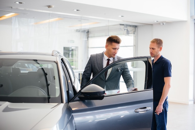 Un jeune homme d'affaires avec un vendeur regarde une nouvelle voiture chez un concessionnaire automobile. Acheter une voiture.
