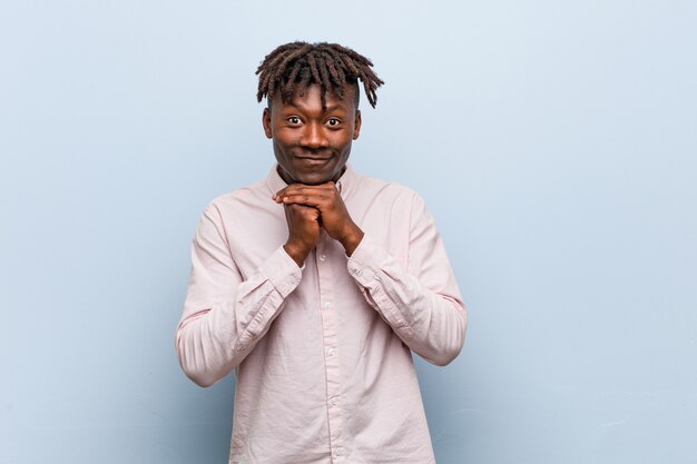 Un jeune homme africain africain garde les mains sous le menton, regarde joyeusement de côté.