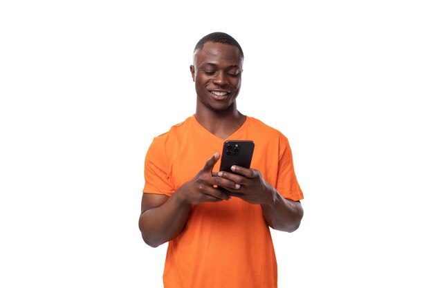 Un jeune homme africain authentique en T-shirt orange se réjouit en lisant des messages sur son smartphone