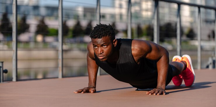 Un jeune homme africain confiant en vêtements de sport faisant des pompes tout en faisant de l'exercice en plein air