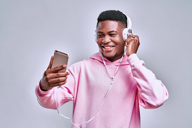 Jeune homme africain dans les écouteurs regardant le téléphone sur fond gris Espace de copie