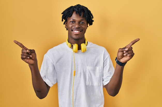 Photo jeune homme africain avec des dreadlocks debout sur fond jaune souriant confiant pointant avec les doigts vers différentes directions copiez l'espace pour la publicité