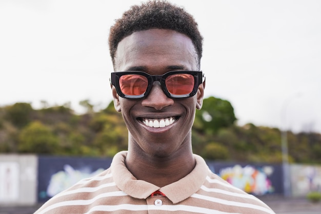 Jeune homme africain avec des lunettes à la mode souriant à la caméra en plein air