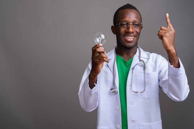 Jeune homme africain médecin portant des lunettes sur mur gris