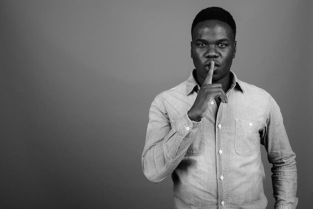 jeune homme africain portant une chemise en jean contre le mur gris. noir et blanc