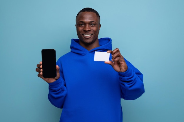 Un jeune homme africain positif avec une coupe de cheveux courte dans des vêtements décontractés avec une carte en plastique paie les achats