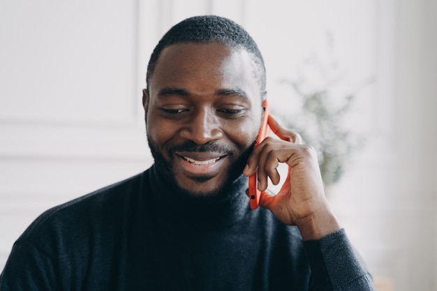 Jeune homme africain souriant ayant une conversation d'affaires sur téléphone mobile