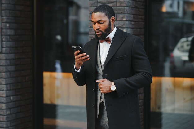 Jeune homme africain en tenue de soirée à l'aide de téléphone mobile