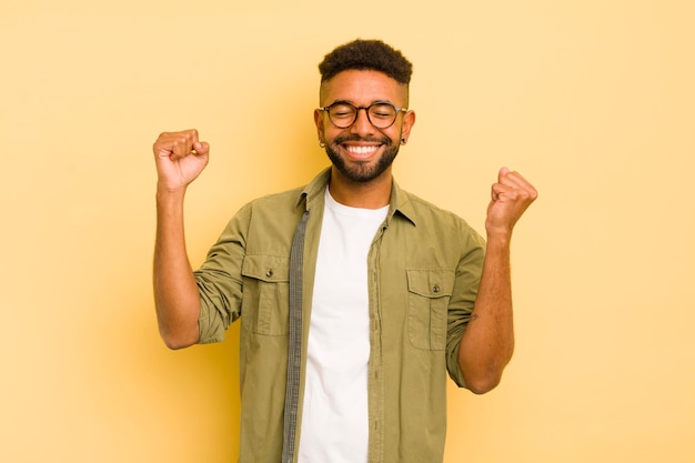 Jeune homme afro à l'air extrêmement heureux et surpris de célébrer le succès en criant et en sautant