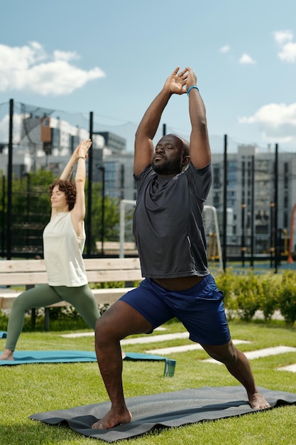 Jeune homme afro-américain actif en tenue de sport debout sur un tapis et faisant de l'exercice