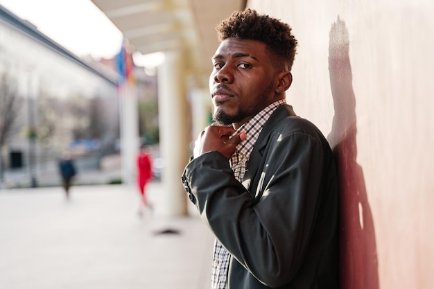 Jeune homme afro-américain ajustant le col d'une chemise à carreaux regardant la caméra