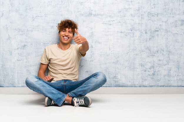 Jeune homme afro-américain assis sur le sol avec le pouce levé parce qu&#39;il s&#39;est passé quelque chose de bien