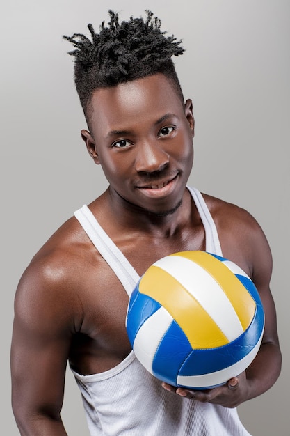 Jeune homme afro-américain athlétique avec ballon de volley-ball en regardant la caméra