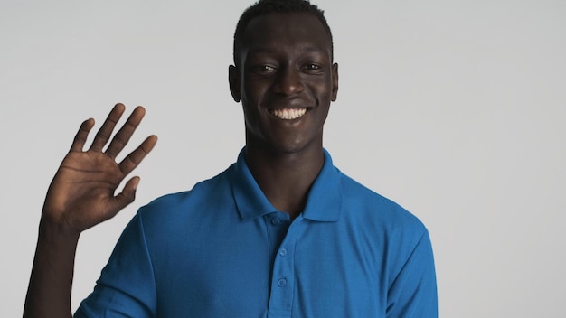 Jeune homme afro-américain attrayant amical agitant la main bonjour à la caméra sur fond gris Expression de salutation