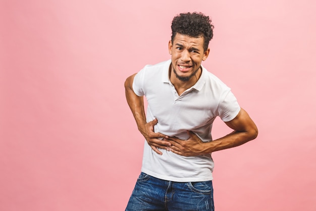 Jeune homme afro-américain aux cheveux afro isolé sur fond rose avec la main sur le ventre, une maladie douloureuse ne se sent pas bien.