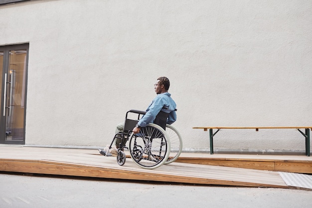 Jeune homme afro-américain aux jambes paralysées assis dans un fauteuil roulant et déménageant dans une maison avec rampe pour fauteuil roulant