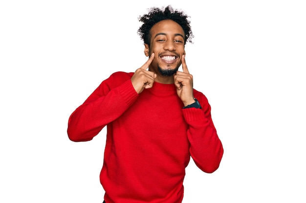 Jeune homme afro-américain avec barbe portant un pull d'hiver décontracté souriant avec les doigts de la bouche ouverte pointant et forçant un sourire joyeux