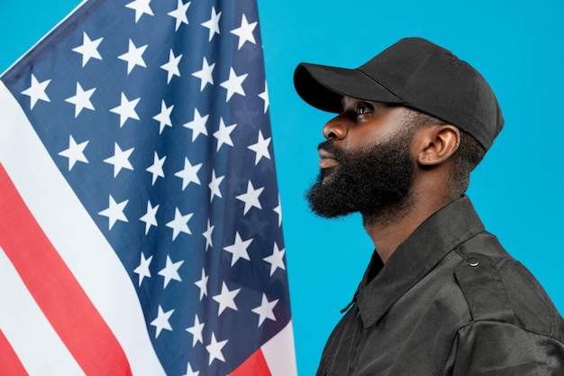 Jeune homme afro-américain barbu en uniforme noir et casquette debout contre le drapeau étoilé