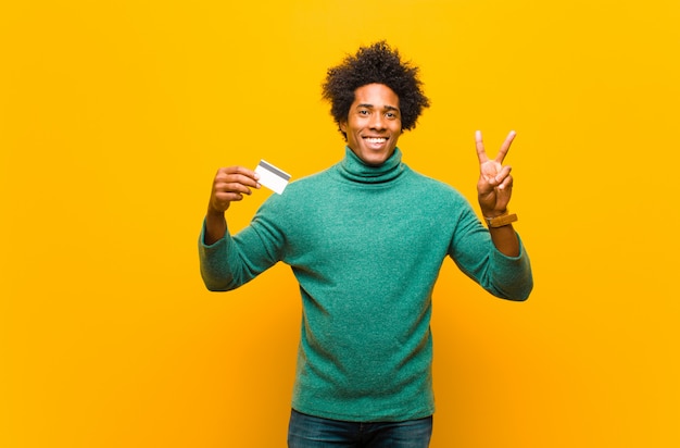 Jeune homme afro-américain avec une carte de crédit contre orange