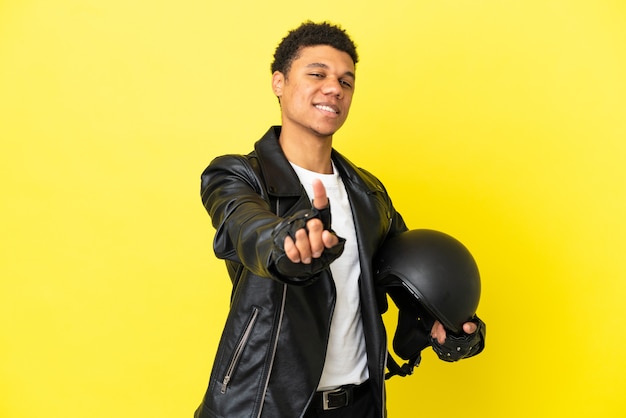 Jeune homme afro-américain avec un casque de moto isolé sur fond jaune montrant et levant un doigt