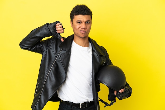 Jeune homme afro-américain avec un casque de moto isolé sur fond jaune montrant le pouce vers le bas avec une expression négative