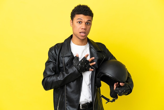 Jeune homme afro-américain avec un casque de moto isolé sur fond jaune surpris et choqué en regardant à droite