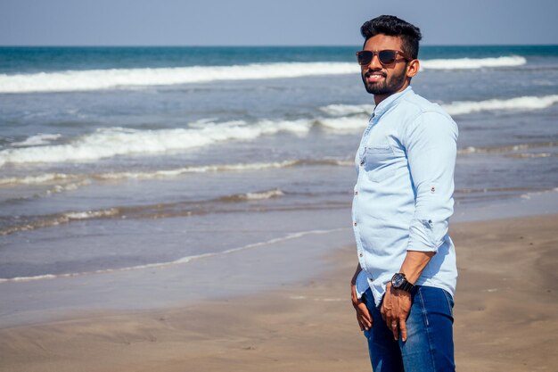 Photo jeune homme afro-américain en chemise bleue et jeans sur la plage de l'océan.