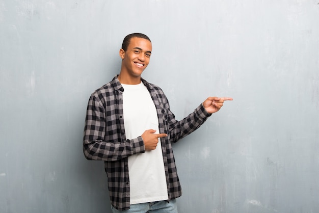 Jeune homme afro-américain avec une chemise à carreaux, un doigt pointé sur le côté en position latérale