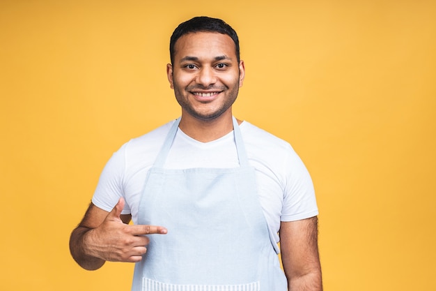 Jeune homme afro-américain cuisinier noir portant un tablier isolé sur fond jaune. Doigt pointé.