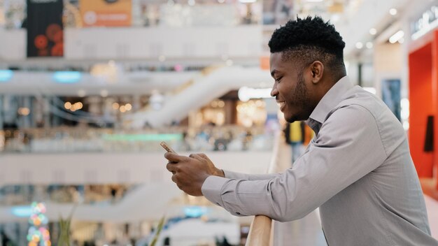 Jeune homme afro-américain dans un centre commercial passant du temps libre sur les réseaux sociaux sur smartphone