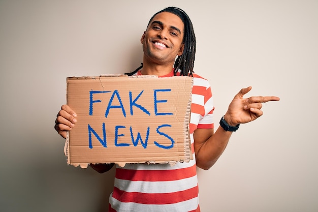 Jeune homme afro-américain avec des dreadlocks tenant une bannière avec un faux message de protestation très heureux pointant avec la main et le doigt sur le côté